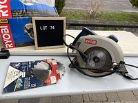 Wide view showing Ryobi circular saw, original box, extra blade in packaging and a letter board stating lot number 74.