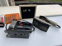 View of lot showing Black and Decker sander with taped sanding surface and Craftsman jigsaw on white surface with lot number sign.