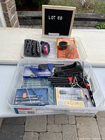 Wide view of plastic bin containing multiple used hand tools including Allen keys, screwdrivers, and a DeWalt bit set in packaging