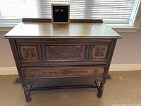 Front view of vintage wooden dresser/sideboard showing carved floral front center panel and decorative metal handles on drawers.