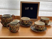 Full set on table with three cups, three matching saucers, creamer and sugar bowl, labeled Lot 10