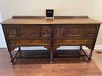 Front view of the large, ornate sideboard showing detailed carved halftone dot floral pattern on the drawer panels, ring pull handles, turned legs, and base stretcher supports. Dark wood finish with patina and age wear.