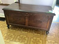 Front and side view of the unbranded cedar chest showing carved decorative panels, turned legs, and carved trim along the bottom edge.