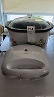 Photo showing Rival crock pot with floral pattern and glass lid and Salton waffle maker in front.