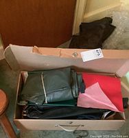 Box containing several folded rolls of vinyl fabric in dark green, black and red shades.