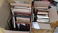 Two cardboard boxes filled with assorted empty picture frames of various sizes and styles stacked vertically and horizontally.