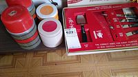 Red and grey stackable thermos, two white plastic containers with colored lids, and Sheffield branded boxed steak cutters and serving utensils