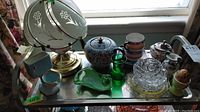 Overview photo of assorted small decor and glass pieces on a shelf, including lamp, vases, jars, and glass bowls.
