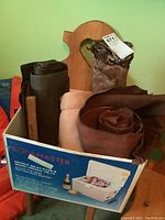 Box containing multiple rolls of leather and suede fabric pieces with different shades of brown and tan.