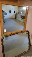Both wood framed mirrors displayed leaning against a wall, showing their sizes and frame styles