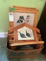 Box containing multiple wood-framed wildlife prints with some visible print paper wear, showing a frame of two kingfisher birds and several other prints behind.
