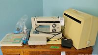 Photo showing Kenmore sewing machine with accessories including carrying case, instruction booklets, foot pedals, and small bottles.