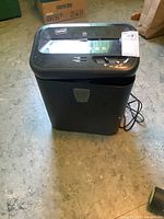Front view of the Staples paper shredder on a concrete floor showing overall shape and pull-out bin.
