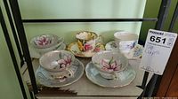 Five ceramic tea cups and matching saucers on shelf with floral patterns and some gold trim visible