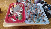 Two trays of multiple small Wade ceramic figurines and other small decorative animal and character figurines laid out on tables.