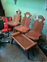 Three solid wood chairs with heart-shaped backrests and small wooden tray table with foldable legs in front.