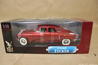 Side view of the red 1948 Tucker diecast model car in sealed display box showing scale and branding.