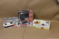 Photo showing all three items boxed: George Foreman Grill, Alligator Onion Slicer, Chef's Choice Sharpener