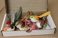 Nine decorative birds in a cardboard box showing various colors and feather details