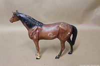 Side view of brown cast iron horse figurine showing black mane and tail with paint chipping and wear on body surfaces.