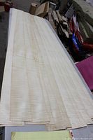 Full view of 15 thin veneer sheets stacked, showing light natural wood with curly grain patterning.