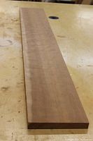 Long view of figured Cherry wood board on a workbench, showing surface grain and color.