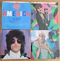 Top view of the four 45 rpm vinyl record sleeves featuring cover art from Prince and the Revolution singles 'America,' 'Pop Life,' 'Raspberry Beret,' and 'When Doves Cry.'