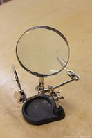 Magnifying glass and stand with two adjustable clips on black base, showing full unit and clear magnifying glass lens.