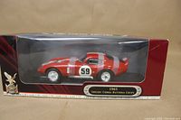 Front side view of the factory-sealed boxed 1965 Shelby Cobra Daytona Coupe model with red body and white stripes, showing car on side with number 59 decal.