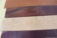 Four thin exotic wood pieces laid flat on table surface showing their colors and grain patterns