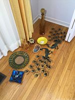 Photo showing entire lot laid out on floor including tall amber decanter, metal peacock wall hangings, various glass bowls, dishes, and barometer.