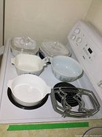 Two Corning Ware baking dishes with glass lids on the stove, along with a Pyrex mixing bowl and three metal burner stands.