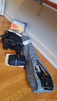 Binoculars, camera case, and Kodak lens hood box arranged on floor with tripod case to side.