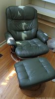 Full view of green leather-like reclining chair with visible wear and matching ottoman on wooden bases.
