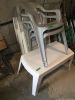 Stack of white folding resin chairs on top of white resin coffee table, showing size and model of table and chairs