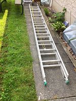 Full view of the aluminum extension ladder laid out on a concrete and grass surface showing its full length and condition.