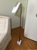Full view of lamp showing silver shade, brass-tone pole and white marble base on hardwood floor.