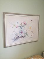 Full view of the framed floral oil painting on canvas, hanging on a light green wall.
