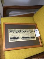 Framed ink on paper artwork placed on a yellow chair, showing full piece in wooden frame.