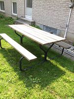 View of picnic table from side showing metal frame and wooden planks on tabletop and bench seat.
