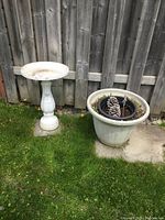 Full view of resin birdbath standing next to the large resin planter placed outdoors by a wooden fence