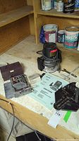 Photo showing the Craftsman router, manual, several attachments, and bits laid on a wooden work surface with paint cans in background.