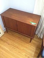Angled front view of teak cabinet with two roll-back doors and tapered legs