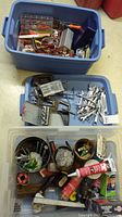 Two totes filled with various hand tools, adhesives, batteries, and hardware parts including wrenches, cutters, and clamps