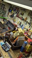 Workbench with pegboard showing various hand tools like screwdrivers, pliers, hammers, pipe wrench, clip-on light, and small hardware items arranged