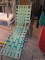 Front view of vintage aluminum framed outdoor lounger with green and white woven webbing showing wear and fraying straps.