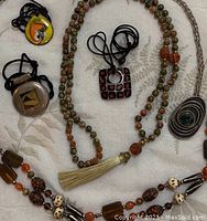 Overview of all six necklaces including the double strand and tassel, various pendants, and bead styles shown on a white fabric background.