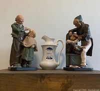 Photo of two figurine statues and a central white advertising pitcher labeled Dr Patch's treatment pitcher.