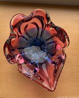 Top view of a multicolored art glass bowl showing red and blue hues and organic shape with clear glass elements.