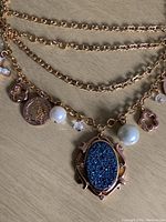 Close-up photo of gold-tone chain with blue druzy centerpiece and various charms including pearls and coins.